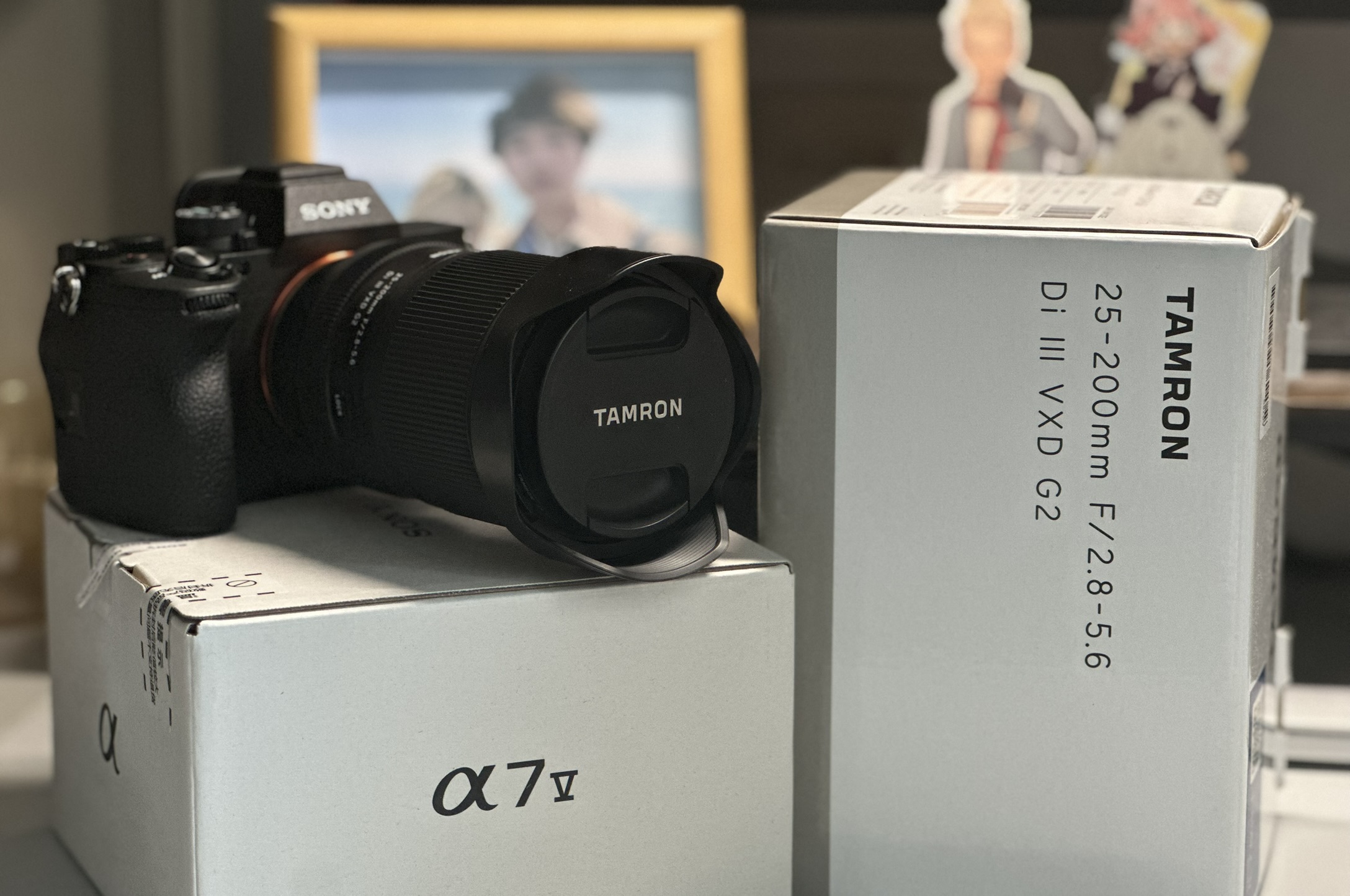A Sony α7 V camera with a Tamron zoom lens resting on its box, beside the box of the Tamron 25-200mm lens.